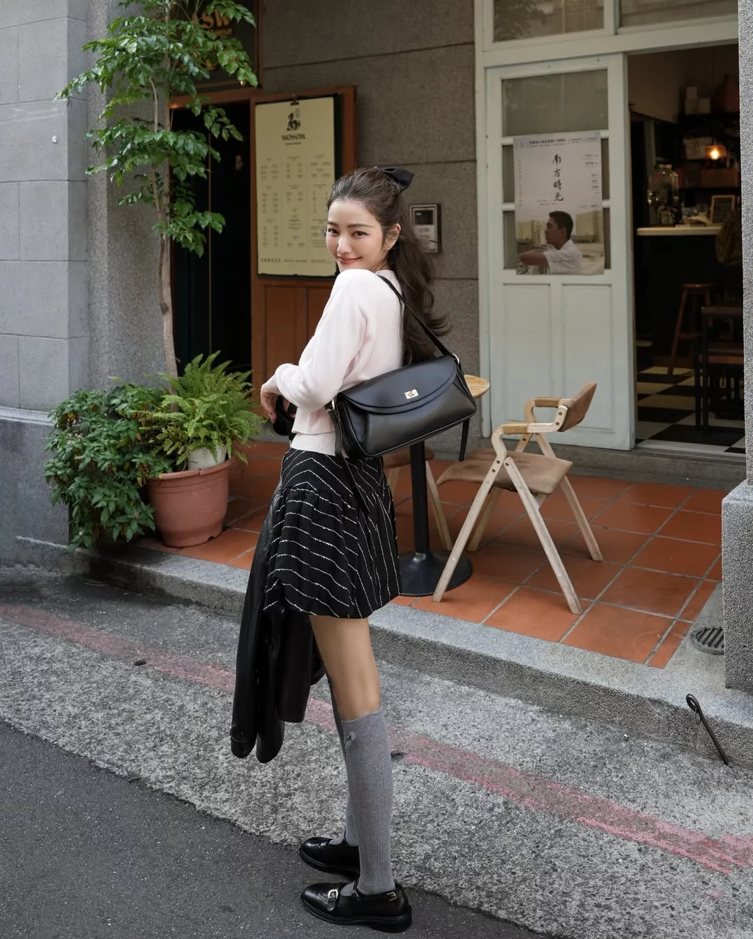 想把少女感單品穿得時髦而不顯幼稚，關鍵在於單品之間的風格平衡。許路兒以 Sandro 的黑色皮革外套搭配條紋澎裙，利用皮革的俐落與硬挺質感，為裙裝的輕盈輪廓增添一點率性。內搭簡潔粉色針織上衣讓整體線條保持乾淨，而灰色長襪與瑪莉珍鞋則帶出淡淡的學院氣息，也讓腿部比例看起來更加修長。這種帥氣單品與少女元素的混搭方式，能讓造型既有層次，又保留輕盈感。包款部份，她選擇的是同樣來自 Sandro 的 Le Mambo Shoulder Bag，這款肩背包以平滑皮革打造，搭配簡約弧形翻蓋與金屬旋轉扣設計，線條俐落又帶點復古氣息。包身比例修長，容量實用，既能肩背也能斜背，十分符合日常穿搭需求。當整體造型已經有澎裙與長襪等細節時，這種設計簡潔的包款反而更能穩住視覺焦點，也讓整體風格看起來更加耐看。