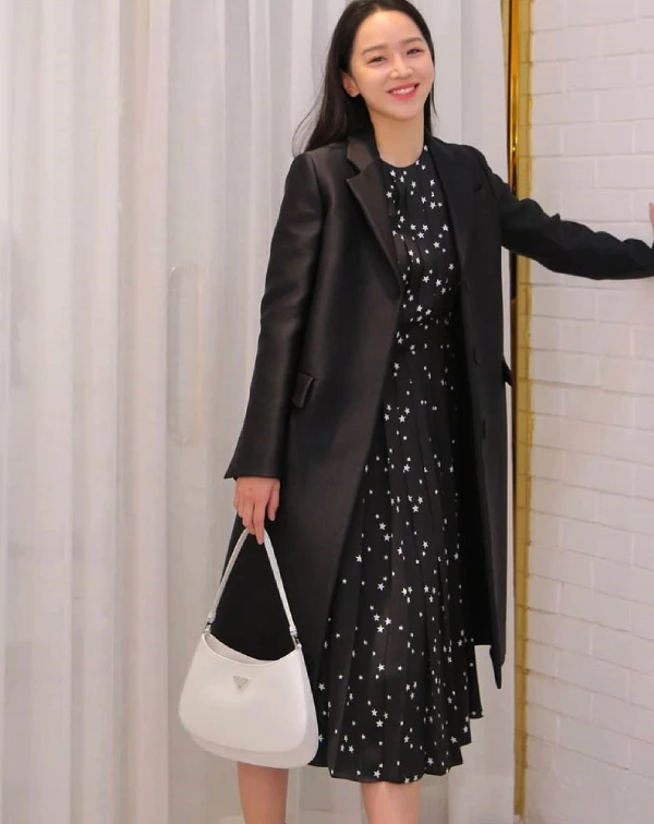 申惠善簡直是「人間Prada」的親善大使吧！手中那只白色的「Cleo」包款，憑藉其標誌性的弧形結構與拋光皮革的細膩光澤，在沉穩的全黑穿搭中，躍然而出，成為視覺的核心。「Cleo」包款那種融合了90年代復古極簡線條，與申惠善清冷而精緻的氣質完美契合，即便只是靜靜站立，也散發出一種高級且不費力的時尚感。