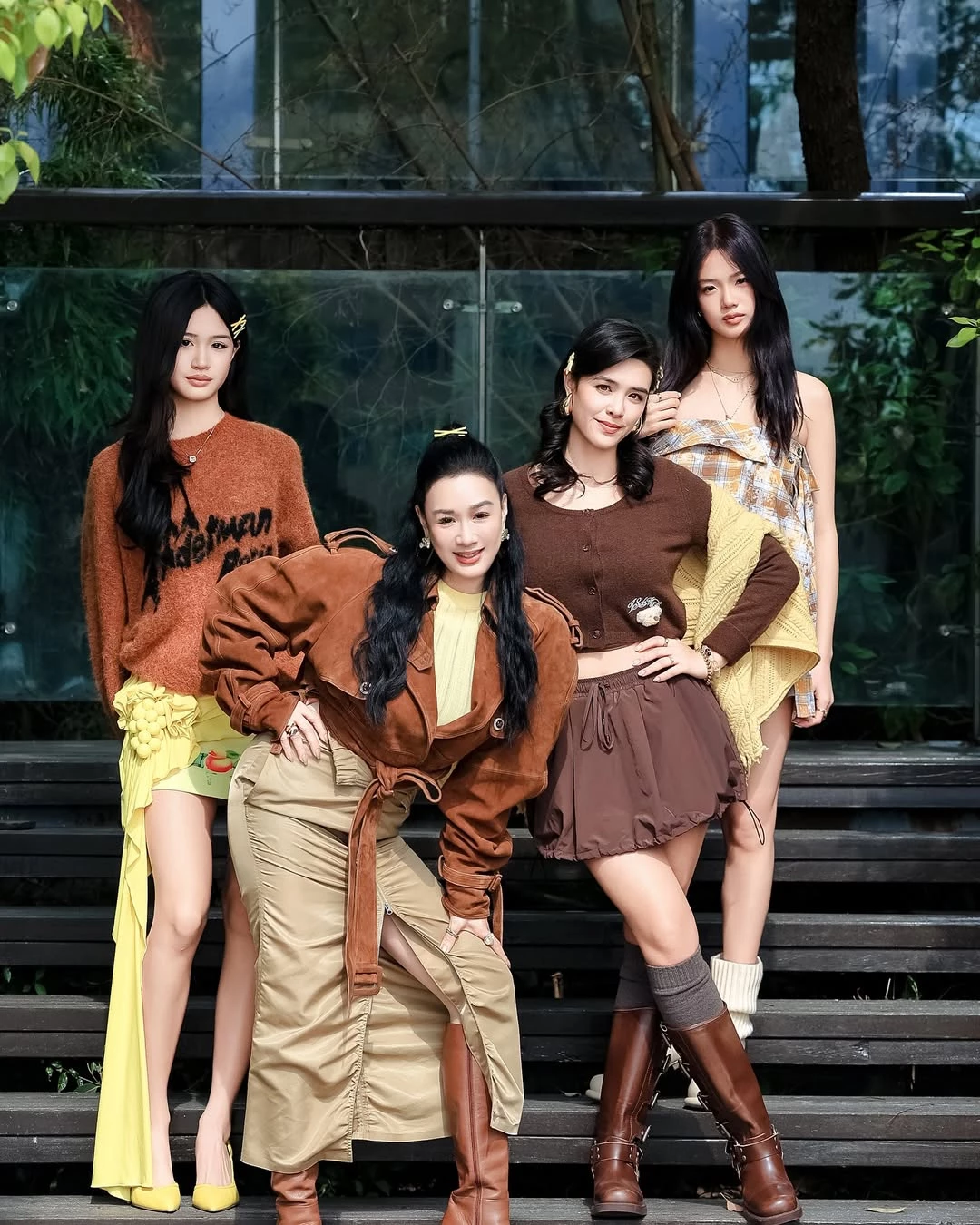 大女兒 Yasmine（右二）這套造型，示範了如何用「同色系深淺變化」把比例穿得乾淨又俐落。深棕色短版針織上衣在胸下位置自然收尾，清楚點出腰線，視覺上直接拉長下半身比例；下身搭配淺棕色高腰泡泡裙，利用蓬度與份量感，反襯腿部線條的纖細修長。腳上的中筒靴搭配襪子，刻意在腿部下緣做出層次切分，既增加造型份量，也讓腿部線條更集中向上延伸。整體落在溫潤的大地色系，成熟卻不厚重，再加上短裙長度拿捏得宜，讓露腿比例成為視覺焦點。這種「短上衣＋高腰裙」的組合，是最不費力的顯高公式，也很適合想穿出氣場、卻不想過於用力的場合。