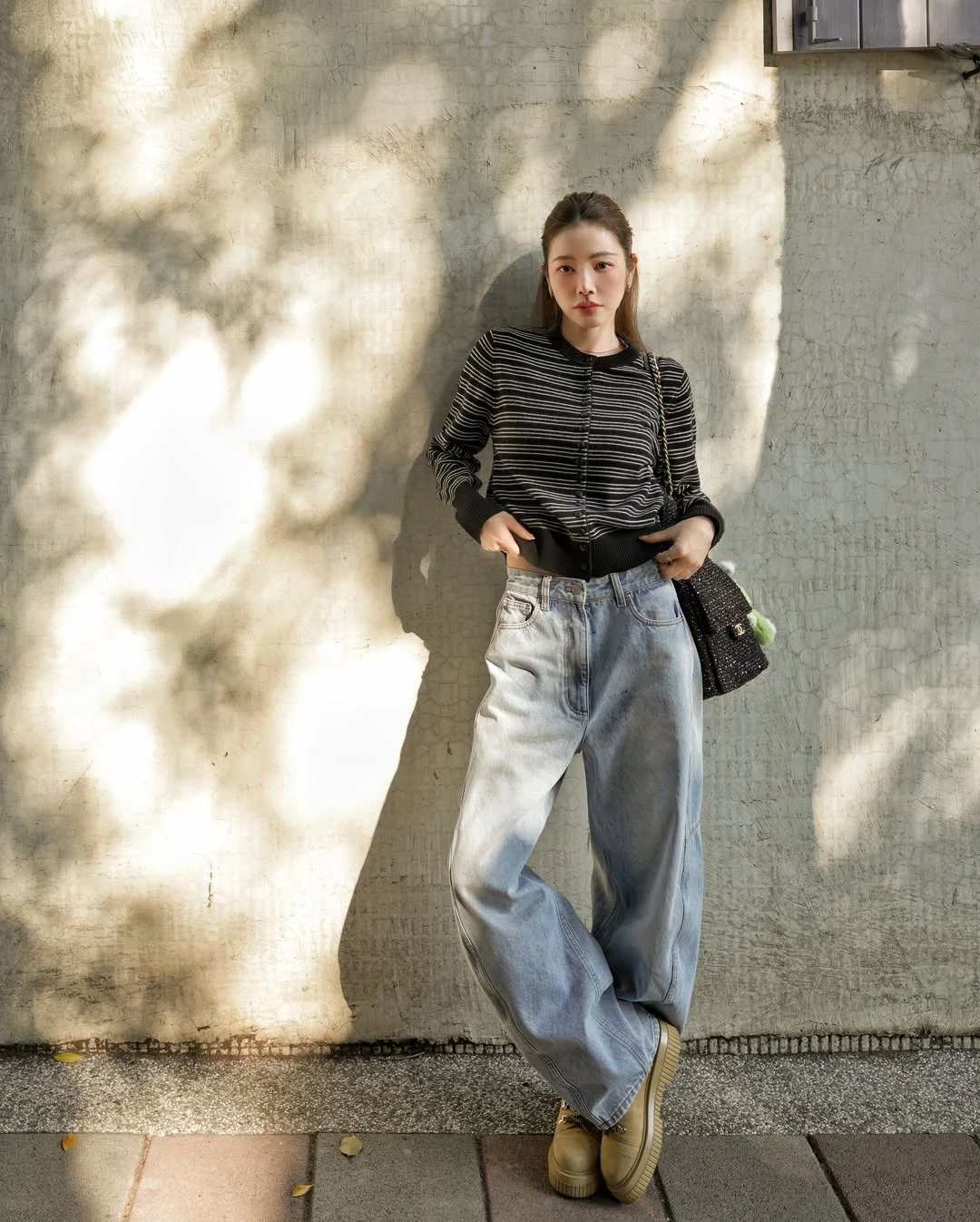 丹寧向來是最容易穿出年輕感的單品，而許路兒很懂得利用「比例」來放大這個效果。她以上海設計師品牌 Slo 的黑色細條紋短版針織上衣搭配高腰寬版牛仔褲，透過短上衣強調腰線，同時讓下半身比例看起來更修長。寬版褲型則帶來一點隨性與鬆弛感，不會過於貼身，也讓整體輪廓顯得更輕鬆。腳下搭配厚底短靴，進一步拉長腿部比例，也為造型增加份量感。這套造型的另一個亮點，是她肩上的 Chanel 25 Tweed Bag，黑色斜紋軟呢材質讓整體更有質感，也呼應上身的黑色調。對於想穿出減齡感的女性來說，這套穿搭非常值得參考，既時髦大方，同時保有青春活力。