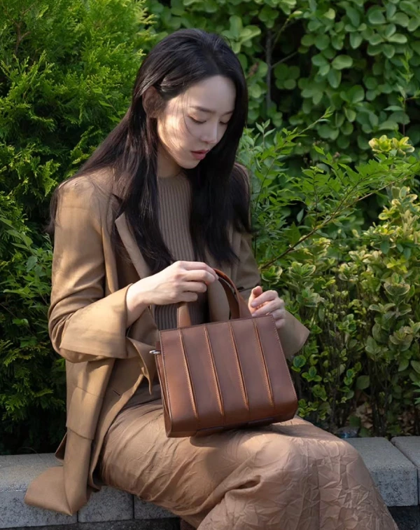 在這張私著照片中，申惠善以一身高級感的焦糖色系穿搭，完美襯托出Max Mara最具標誌性的「Whitney」包包系列。此一系列包款，在2025年之際才迎來深具意義的10週年里程碑，其設計靈感就如同包名，源自於紐約的「惠特尼美國藝術博物館」，包身獨特的線性凹槽，不僅精準模仿了博物館的前衛外牆，更展現了建築美學與頂級皮革工藝的結合。