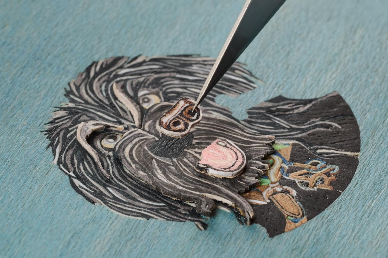 黑白相間的 Orson，是三款裡最有「拼圖靈魂」的一款。牠的臉部、毛流、鼻尖到吐舌的神情，全由8種不同木材切割、打磨、上色再細緻拼接而成。遠看可愛，近看卻是工匠級難度：每一片木材都要順著毛流方向裁切，再以微米等級的精準度貼合，光影才會像真毛一樣自然。搭配錶盤旁那根皮革小骨頭，整體就像一幅被縮小的肖像畫。