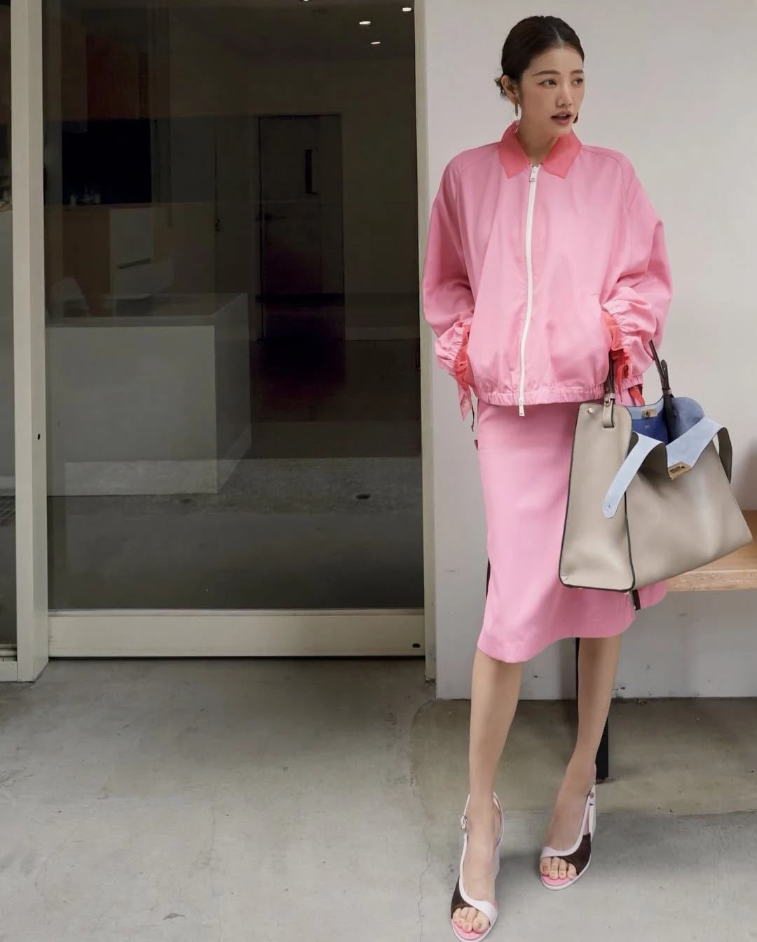 想讓造型看起來更年輕，顏色往往是關鍵。許路兒以 Fendi 粉色拉鍊外套搭配同色系半身裙，利用整體一致的色調營造輕盈感，讓視覺更顯清爽俐落。粉色雖然帶有甜度，但她選擇偏俐落的運動風剪裁，讓造型在柔和與率性之間取得平衡。下身以簡潔拼接設計的高跟涼鞋延伸腿部線條，使整體比例更顯修長。包款則選擇2026春夏大秀全新亮相的 Fendi Way Bag，這款新作以優雅俐落的梯形輪廓搭配雙色皮革設計，外層為低調的鴿灰色，內裡則帶有電光藍的亮點，在極簡之中保留一點驚喜。包身容量實用，線條又十分俐落，既能搭配日常造型，也能延伸到工作場合。對於希望在成熟氣質中保留活力感的女性而言，這種亮色服裝搭配極簡包款的組合，往往能讓整體看起來更精神，也更具現代感。