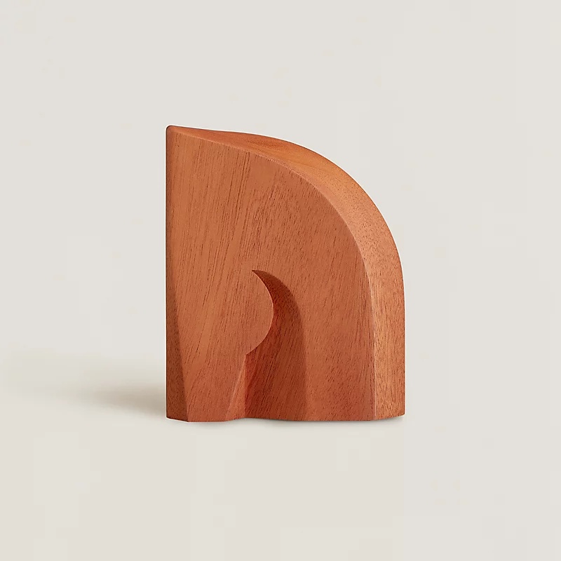 Alezan 書擋以實心桃花心木製成，線條簡約卻帶有裝飾藝術風格的曲線。其名稱來自馬匹棕褐色的毛色，呼應 Hermès 的馬術淵源。