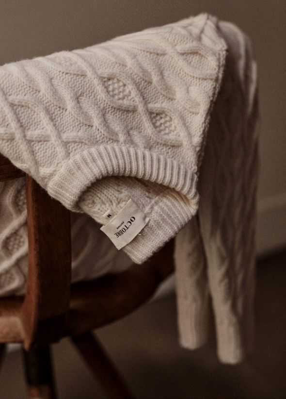 一件深色毛衣懸掛在木製椅上，搭配自然光線與乾淨背景，營造高級毛料的質感氛圍