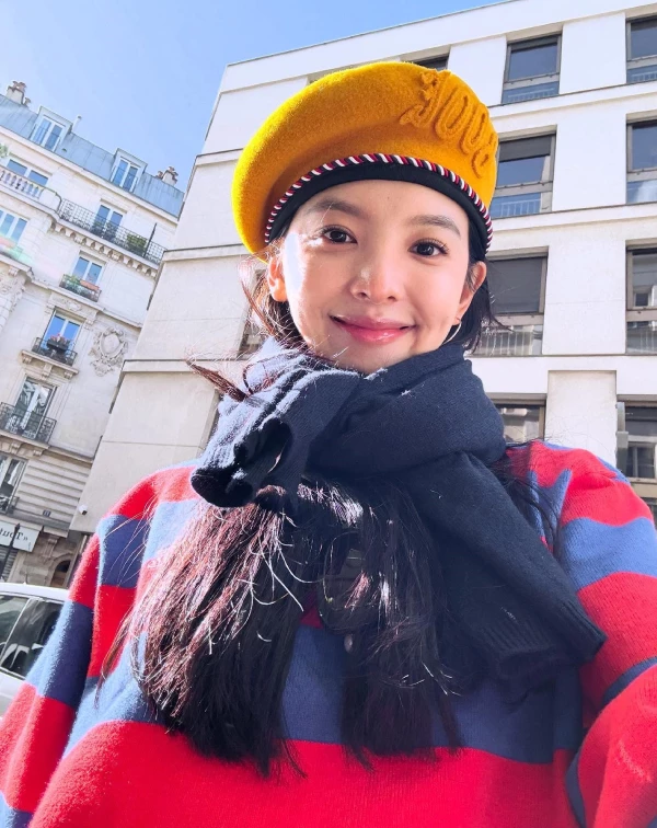 什麼叫作「冬末春初的甜美暴擊」！章若楠這套造型最迷人的地方，莫過於那大膽又充滿生命力的色彩碰撞。在明媚的暖陽映照下，她選用了一頂明度極高的薑黃色貝雷帽，配上身著的紅藍橫條紋針織衫，看似衝突，卻出奇地和諧可愛，洋溢著復古又俏皮的美式校園感，整個人散發出一種鄰家女孩般的親切感與初春朝氣，顯得特別靈動且生動。