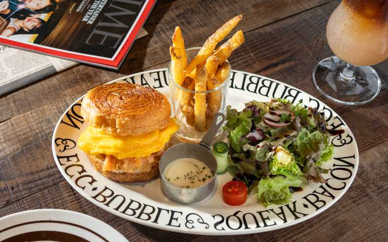 「煙燻鮭魚可頌堡」於可頌表層刷上楓糖，讓香氣與酥脆度更加倍，鮭魚的油脂香氣也適合與清爽的咖啡搭配。（附薯條與沙拉250元，圖／楊澍攝）