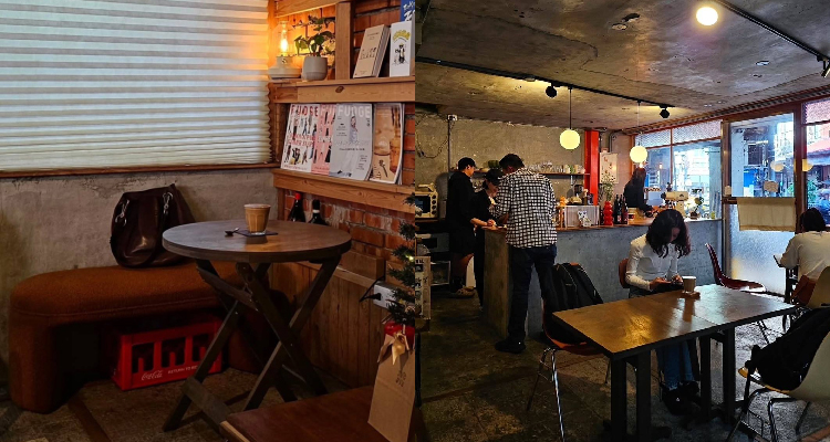 從我這個選座的視角，得以看到咖啡師忙碌穿梭的工作身影，也能捕捉客人推門而入的瞬間。午後的光線柔和地灑進室內，伴隨著客人們自在地聊天聲、咖啡機運作的聲響與香氣瀰漫，讓整個空間凝住在靜謐裡。