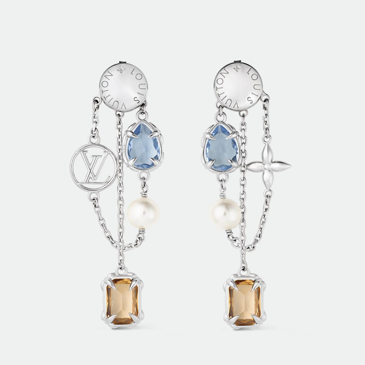 路易威登的 Heirloom Pendant 耳環是獻給魅力女性的最佳禮物。它以不對稱鍊帶串連彩色鋯石與樹脂珍珠，一側耳環飾以 LV  Circle 標誌，另一側則綴以 Monogram 花卉圖案，搭配細膩的花卉造型爪鑲，展現出女性的多面與獨特。琥珀與水藍鋯石色調交錯，像晨光與夜幕的交替，柔美卻有力量。無論搭配白襯衫或絲質洋裝，皆能展現不費力的時髦。