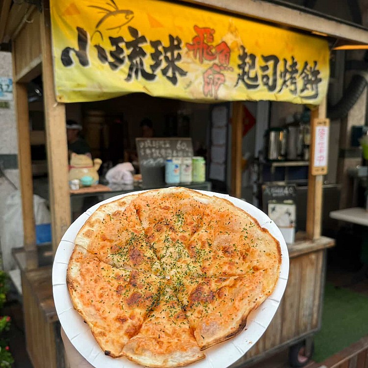 位在小琉球市區的人氣排隊小吃「小琉球飛魚卵起司烤餅」，薄脆餅皮裡包著濃郁起司與會「逼逼波波」的飛魚卵，再加上罪惡感十足的美乃滋，一口咬下薄脆口感的餅皮與鹹甜交織的香氣，讓人一吃難忘。
