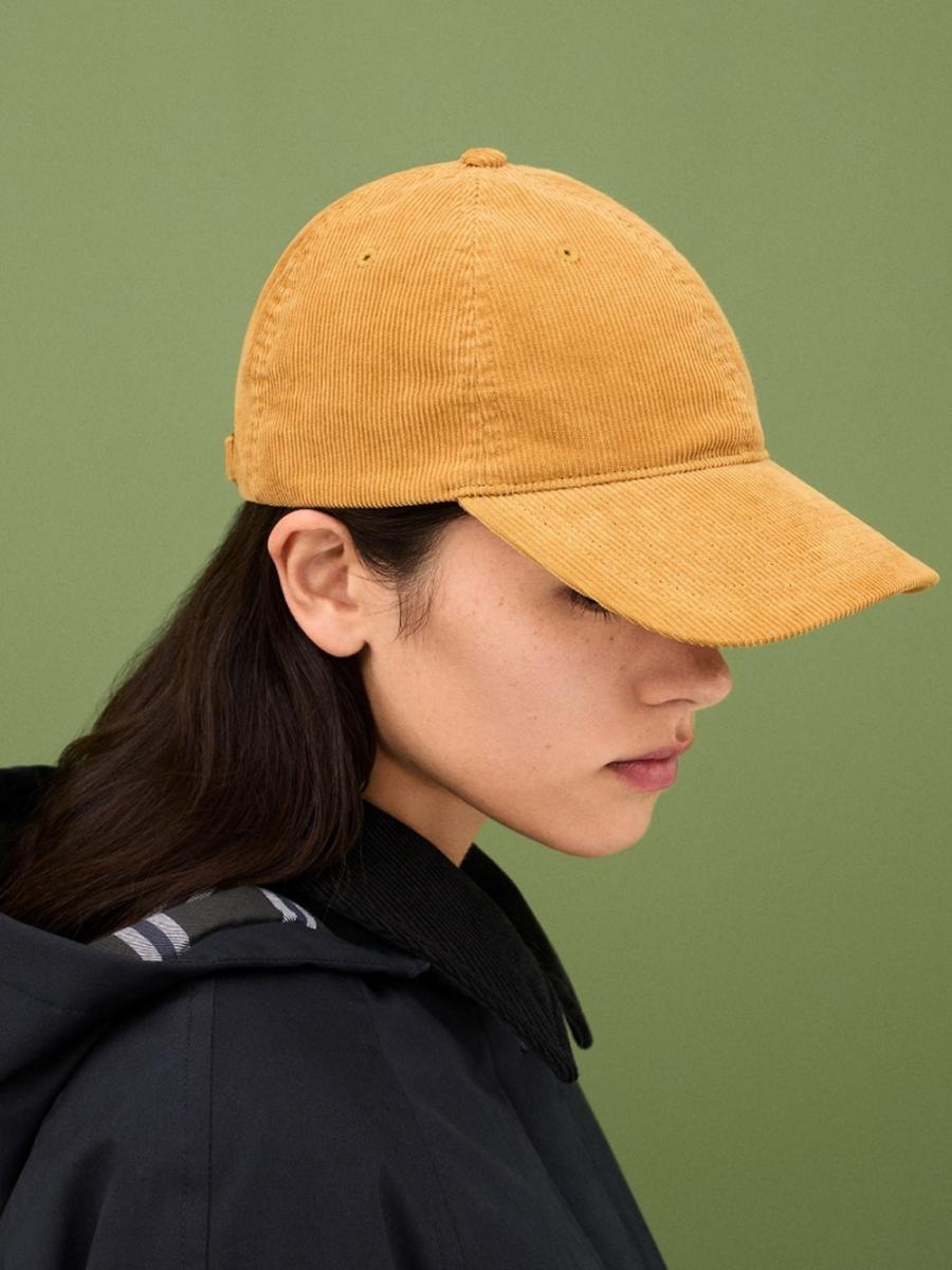 以燈芯絨材質為主的帽款，是本系列中最富「布料語言」的單品之一。帽身搭配腰部可調節扣帶，以及搭扣上的  JW Anderson 標誌，成為視覺焦點。