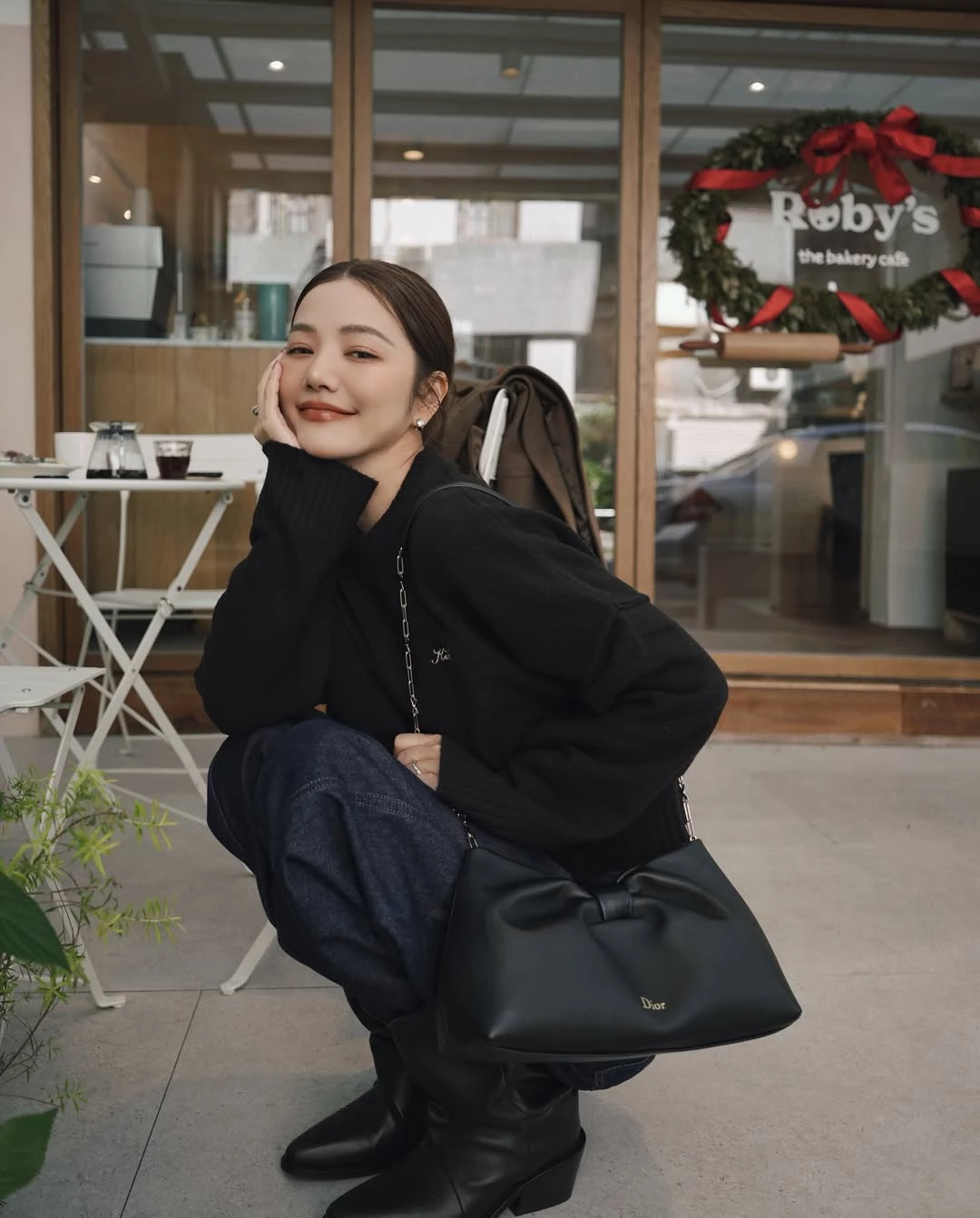 黑色穿搭若搭配得當，其實反而更能凸顯俐落與年輕。許路兒以寬鬆黑色針織上衣搭配深色丹寧褲，整體線條偏向休閒風格，透過寬鬆輪廓營造自然的隨性氛圍。這類造型的關鍵在於「不過度修飾」，反而讓整體看起來更自在，也更符合日常生活的節奏。腳下搭配黑色長靴，使整體線條更顯俐落，也為造型增加一點率性氣質。包款則是 Dior Bow Bag，這款在2026春夏系列登場的新包，以立體蝴蝶結作為視覺焦點，柔軟包身結合細膩皮革工藝，既保留法式優雅，也帶有現代感。黑色款搭配低調金色 Dior 標誌與金屬鏈帶肩背設計，使整體造型在簡約之中多了一點精緻度。當服裝保持低調時，一只設計鮮明的包款往往就能成為整體亮點，也讓日常休閒造型看起來更有層次。